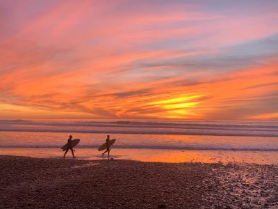 Two surfers walking along the beach at sunset in California.