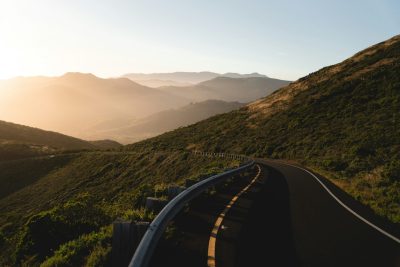 Winding mountain road in California at sunrise with rolling hills in the distance.